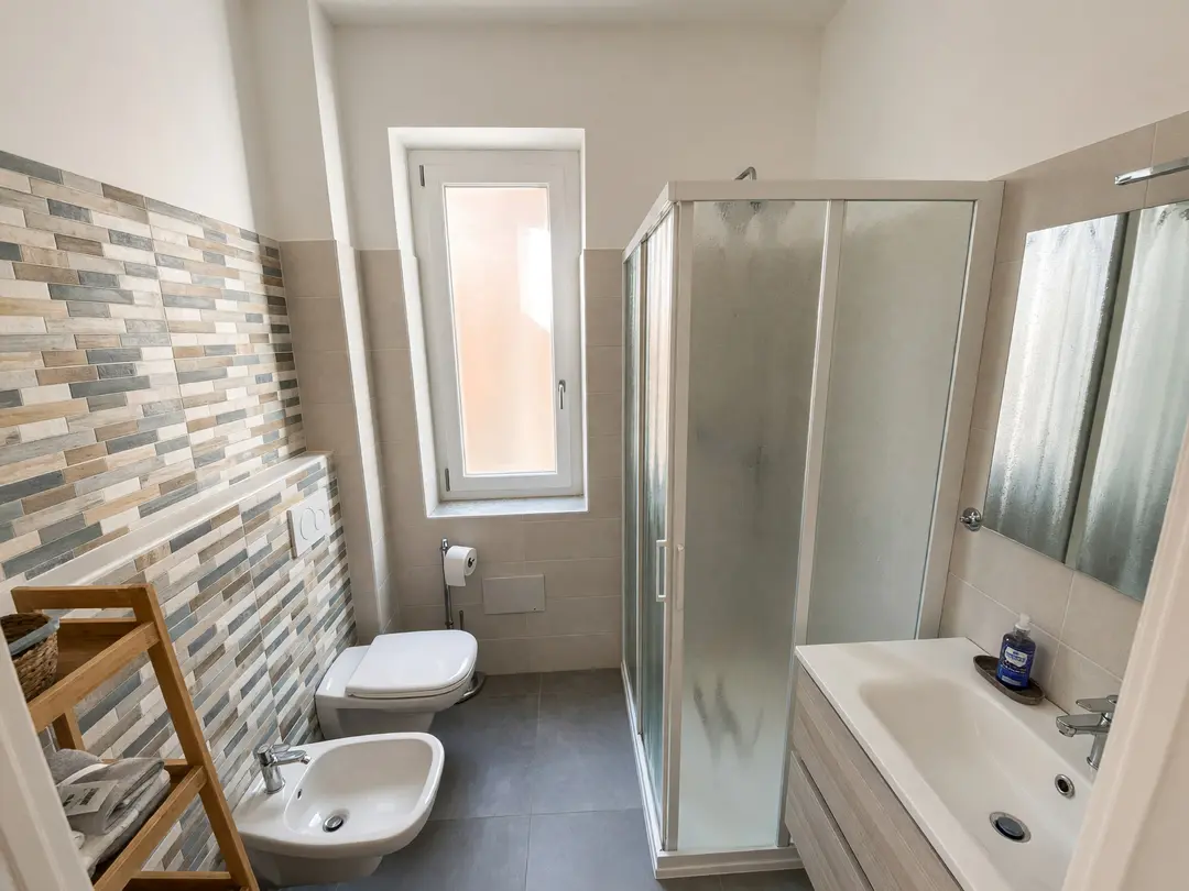 Il bagno con doccia, lavabo, bidet e finestra, rivestito a listelli sabbia e azzurro