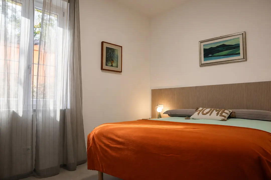 La camera matrimoniale, con il copriletto arancio e la lampada accesa sul comodino