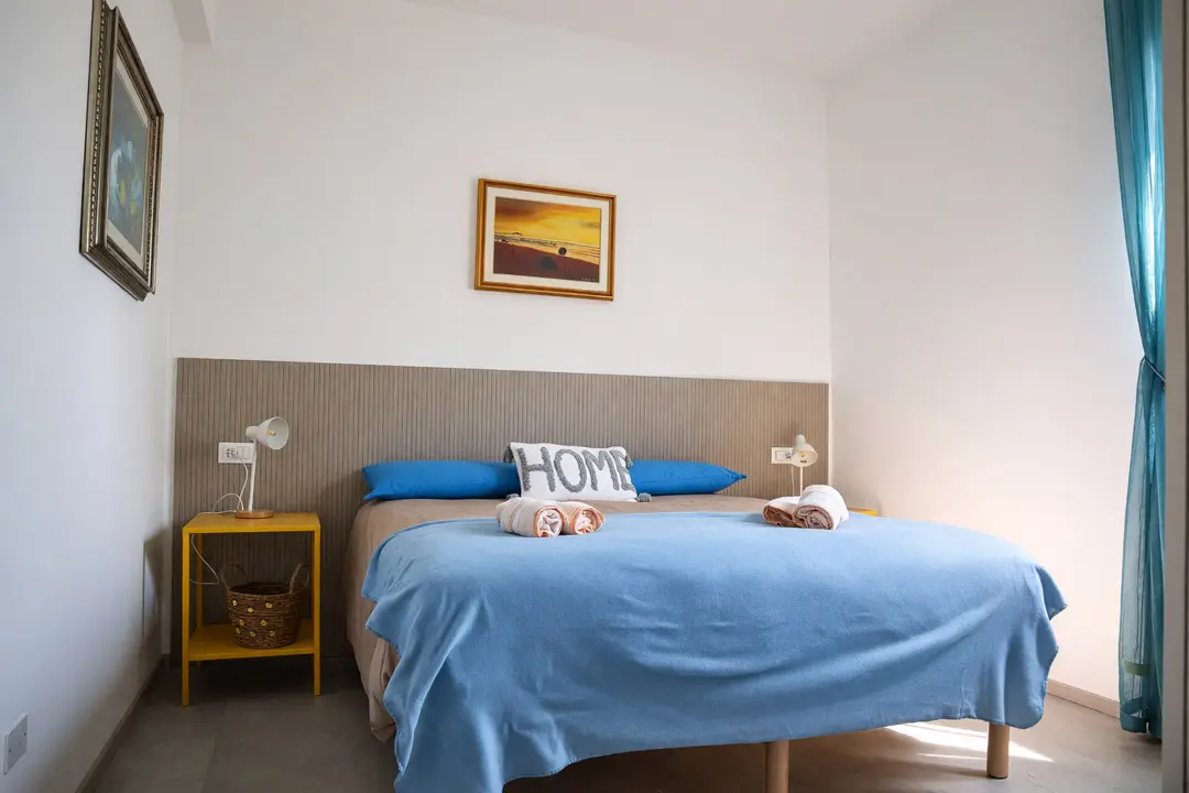 La camera dell’appartamento Limone: il letto matrimoniale con il cuscino “HOME” e i comodini gialli