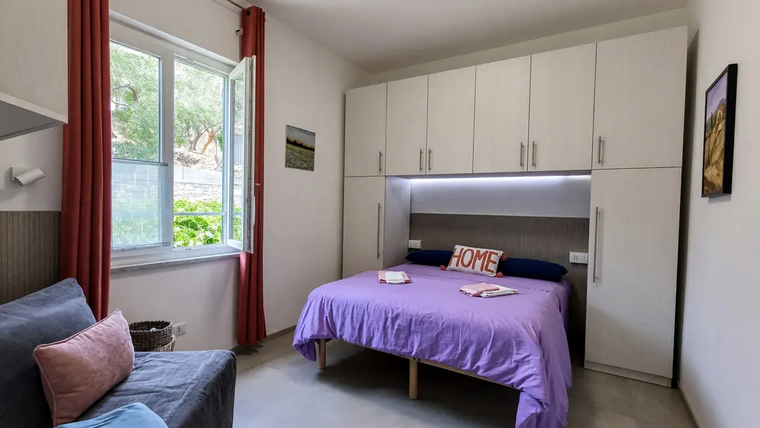 La camera dell’appartamento Lavanda: il letto matrimoniale, la finestra aperta sugli ulivi e la poltrona letto