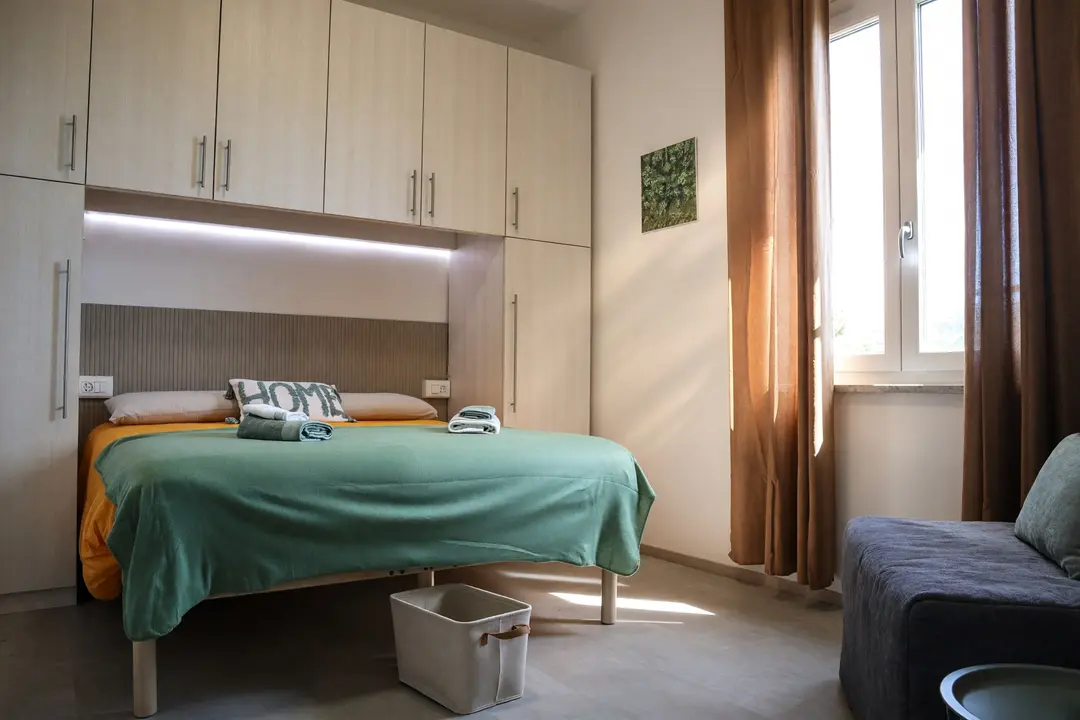 La camera dell’appartamento Ulivo: copriletto verde, armadio a ponte e tende color terracotta