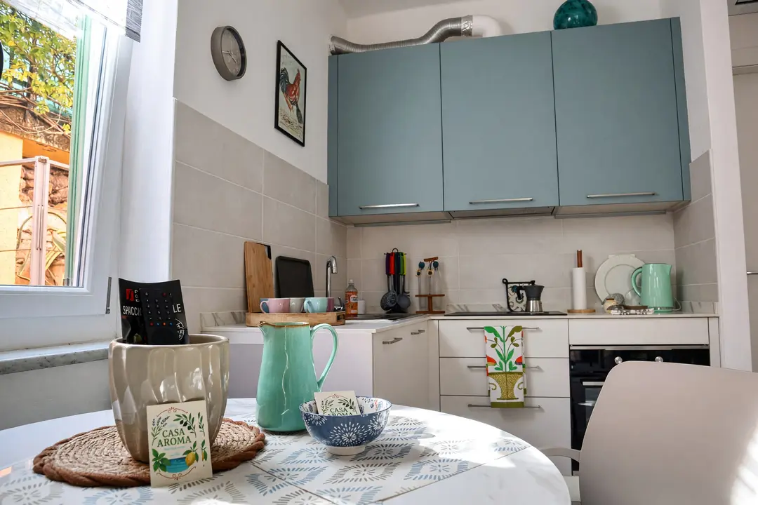La cucina con i pensili azzurri e, sul tavolo, la brocca e il biglietto di benvenuto di Casa Aroma