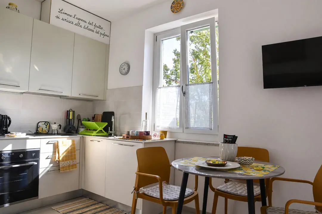 La cucina dell’appartamento Limone: il piano cottura, la finestra e il tavolo con le sedie gialle