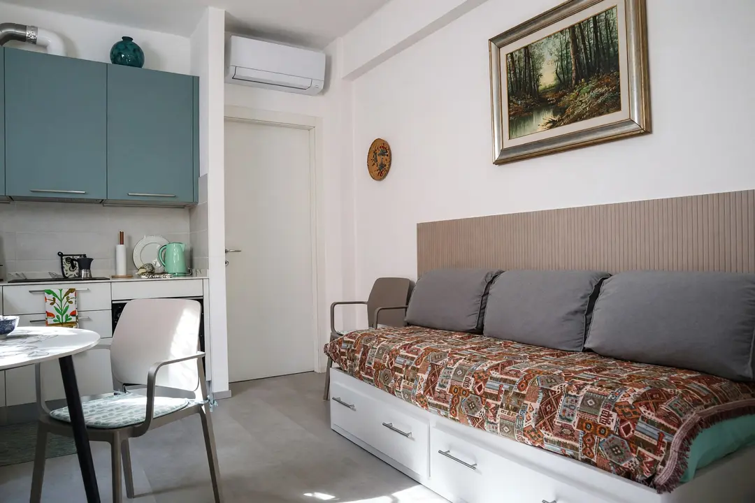 Il soggiorno dell’appartamento Basilico: il divano letto, il tavolo e i pensili verde petrolio della cucina