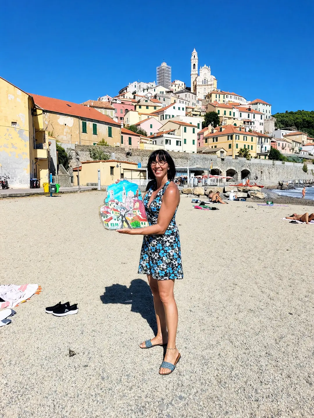 Enrica sulla spiaggia di Cervo con la tegola appena dipinta per il Pennello d’Oro: il borgo, che le sta alle spalle
