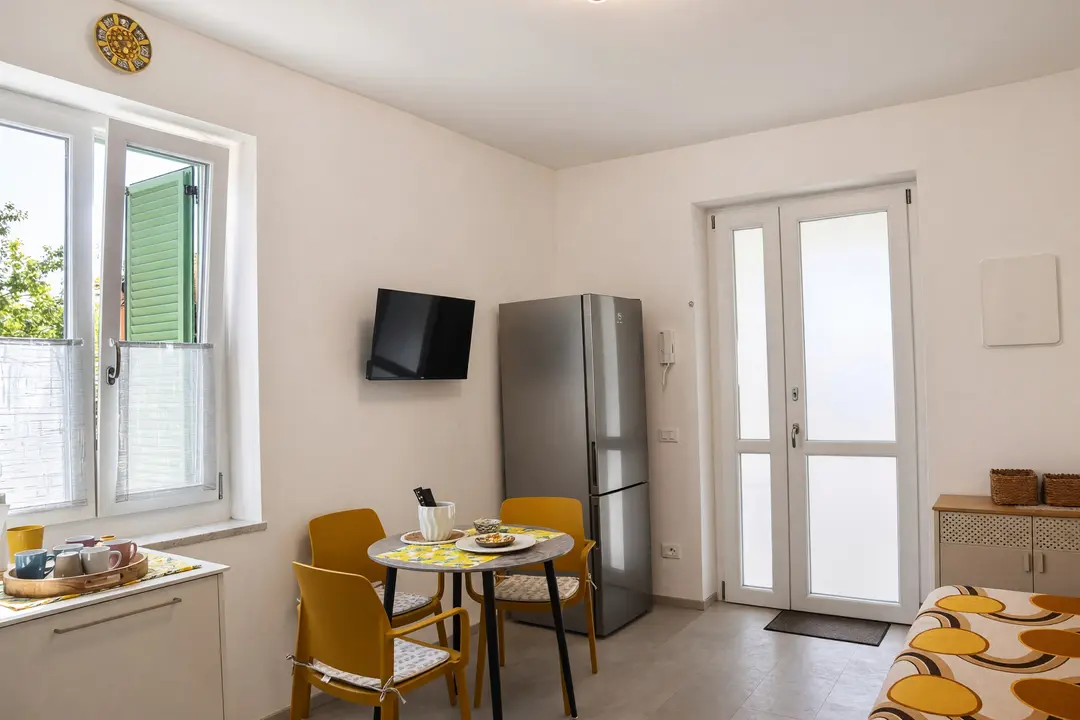 L’ingresso dell’appartamento Limone: la porta vetrata sul portico, il frigorifero e il tavolo apparecchiato