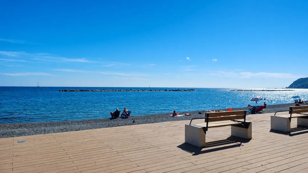 La passeggiata di legno sul mare, con le panchine bianche e la spiaggia di ciottoli