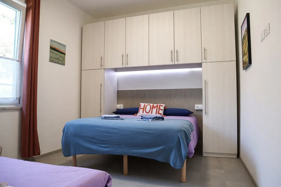 Il letto matrimoniale dell’appartamento Lavanda sotto l’armadio a ponte illuminato, con la poltrona letto aperta a lato