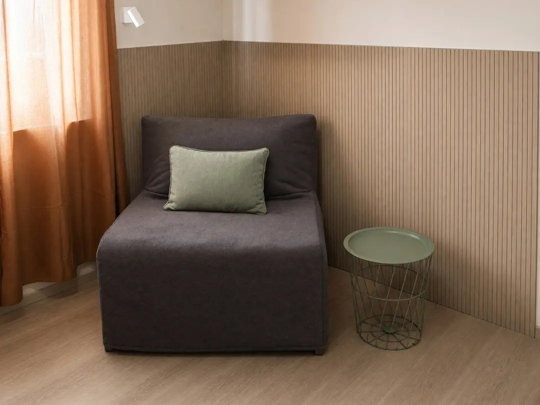 La poltrona letto chiusa nella camera Ulivo, con il cuscino verde e il tavolino, accanto alla tenda color terracotta