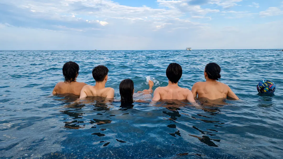 Un gruppo di ragazzi in mare, di spalle, nell’acqua bassa davanti alla spiaggia di San Bartolomeo