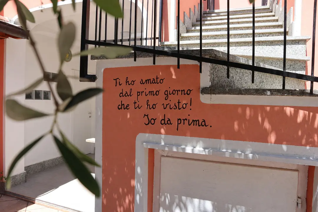 La scritta a mano sul muro corallo della scala, fra le foglie d’ulivo