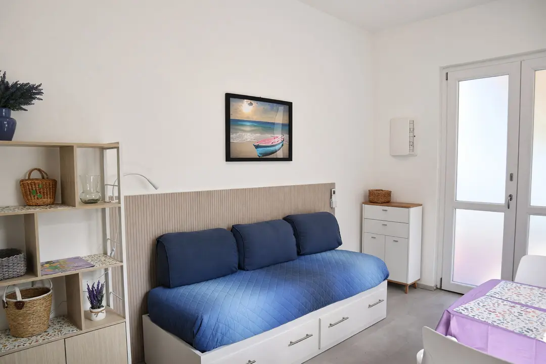 Il soggiorno dell’appartamento Lavanda: il divano letto blu, la libreria e la porta vetrata sul terrazzo