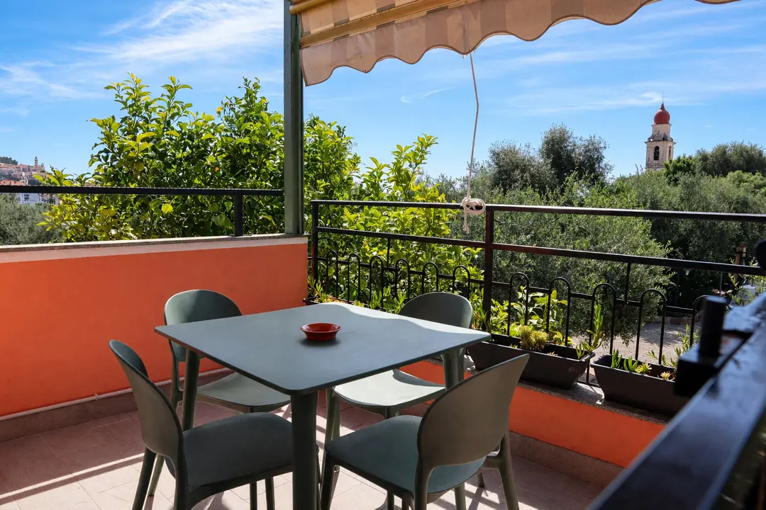 Il terrazzo privato di un appartamento al primo piano: tavolo, sedie e tenda parasole fra gli ulivi